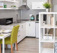 A kitchenette with white furniture and green chairs in a studio apartment.