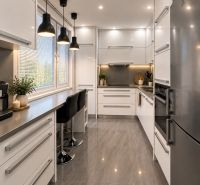 A kitchen in a 3-room apartment with a large window, white cabinets, and bar stools.