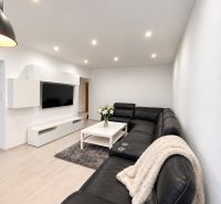 Living room in a 3-room apartment with a large black sofa and a wooden decor floor.