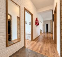 A hallway in a 3-room apartment with a wooden decor floor and mirrors on a brick wall.