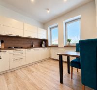 A kitchen with white furniture and a wooden decor floor in a 3-room apartment.