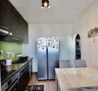 A kitchen in a 3-room apartment with white walls, stainless steel appliances, and a dining table.