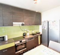 A kitchen with dark cabinets, green tiles, and appliances in a three-room apartment.