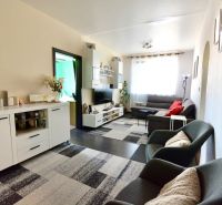 Living room in a 3-room apartment with a sofa, TV cabinet, and armchairs on a floor with a wooden decor.