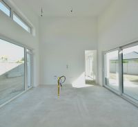 A spacious bright interior of a family house with large windows and an unfinished floor.