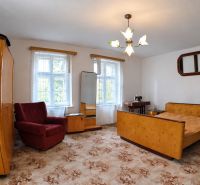 A room in a family house with older furniture, an upholstered armchair, and a floral carpet.