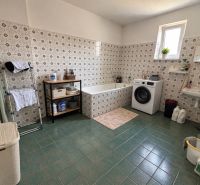 A bathroom in a family house with a washing machine, a bathtub, and green tiles.