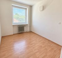 An empty room with a window, wooden floor, white walls, and a radiator.