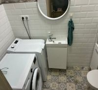 Bathroom with a washing machine, sink, and toilet in a family house with a tiled floor.