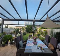 A covered terrace with a dining table and a view of the garden in a family house.