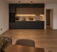 A stylish kitchen with black cabinets, wood-patterned flooring, and lighting in a 3-room apartment.