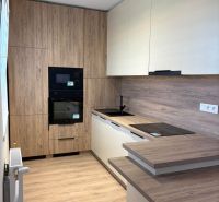 A kitchen in a 2-room apartment with a wooden decor floor and light furniture.
