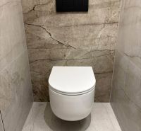 A toilet with a wall-hung WC and stone tiles in a 2-room apartment.