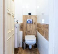 A toilet with a wooden decor floor, a small sink, and white walls.