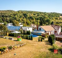 A family house in Potoky, a garden with a swimming pool and lawn, surrounded by trees and hills.