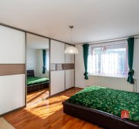 A bedroom in a family house with a sliding wardrobe, green curtains, and a wooden decor floor.