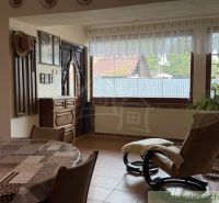 Interior of a family house with an armchair, table, and large windows letting in light.