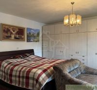 Bedroom in a family house with wardrobes, a bed, and a chair, with paintings on the walls.