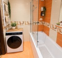A bathroom with a shower and a washing machine in a 3-room apartment, warm orange tiles.