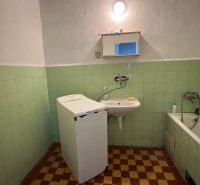 A bathroom with a washing machine, green tiles, and a white bathtub in a family house.