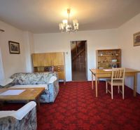 Living room in a family house with carpeted floor, floral pattern, and wooden furniture.