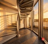 A villa with a spiral metal staircase and large windows overlooking the sunset.
