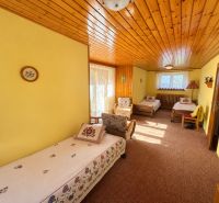 A room in a family house with three beds, a wooden ceiling, and yellow walls.