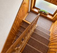 A wooden staircase in a family house with a carpet and a window with decoration.