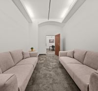 Bright office with two sofas and open doors leading to another room.