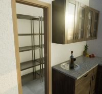 A kitchen in a family house with a pantry, wooden cabinets, fruit, and a granite countertop.