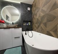 A bathroom in a 3-room apartment with a round mirror, a bathtub, and a decorative wall.