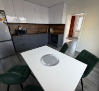 A kitchen in a 3-room apartment with a wooden decor floor, green chairs, white table.