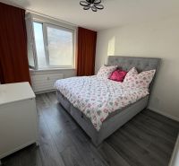 A bedroom with a bed and a wooden decor floor in a three-room apartment.