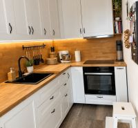 A kitchen with white cabinets, a wooden countertop, and a floor with a wooden decor in a 3-room apartment.