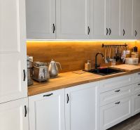 A kitchen with white cabinets, wooden decor, and underlighting in a 3-room apartment.