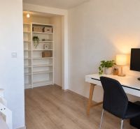 A workspace with a computer and shelves in a 3-room apartment, flooring with a wooden decor.