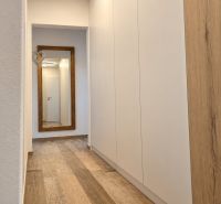 A hallway in a 3-room apartment with a wooden decor floor and a large mirror.