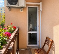 A balcony in a 3-room apartment with air conditioning, wooden chairs, and flowers.