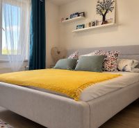 A bright bedroom with a bed, yellow blanket, shelves, and a wooden decor floor in a 3-room apartment.