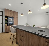 A kitchen with an island, a black countertop, and a wooden decor floor in a two-room apartment.