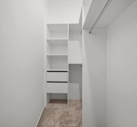 A wardrobe in a 2-room apartment with white shelves and carpeted floor.