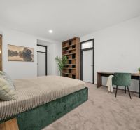 Bedroom with a bed, desk, and plant in a two-room apartment.
