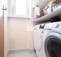Washing machine, dryer, and shelves with cleaning products in the laundry room of a three-room apartment.