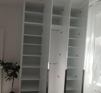 An open white wardrobe in a 3-room apartment with blankets on the bed.
