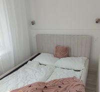 Bedroom in a 3-room apartment with a bed on the floor with a wooden decor, white wall, and curtain.