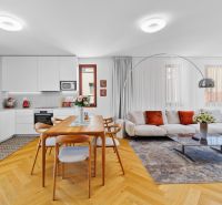 Living room and kitchen in a 3-room apartment with a wooden decor floor and a dining table.