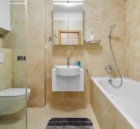 A bathroom in a three-room apartment with a bathtub, shower corner, and tiles in cream tones.