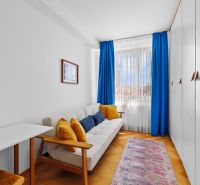 A bright room with blue curtains, a sofa, a carpet, a wardrobe, and a wooden decor floor.
