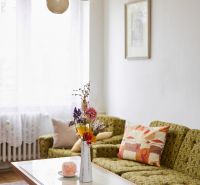 A bright living room in a three-room apartment with a sofa, table, and decorative flowers in a vase.