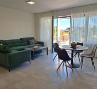 A bright living room with a large sofa, dining table, and a view outside in a two-room apartment.